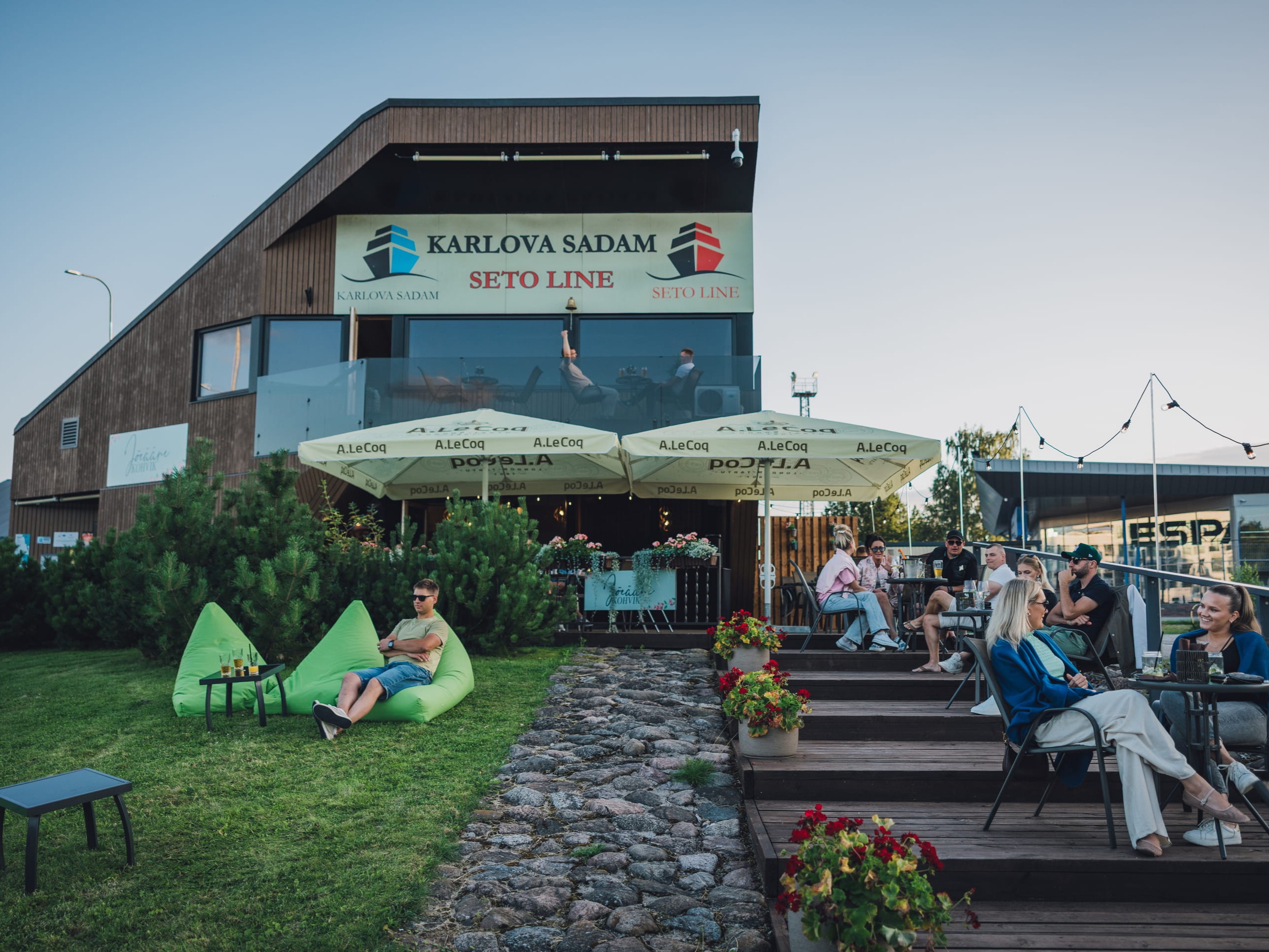 Õhufoto Jõeääre kohvikust ja terrassist Karlova Sadamas, päikesepaistelisel päeval õues istuvate külalistega.